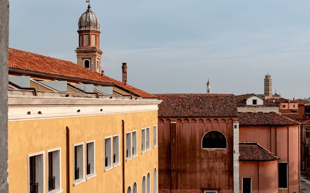 Elegant Italian palazzo hotel with ornate balconies, terracotta facade, and lush greenery, overlooking a picturesque Venetian canal at golden hour