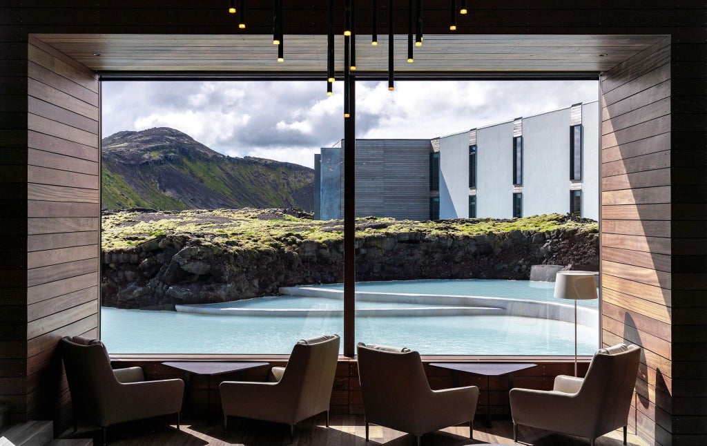 Luxurious minimalist hotel nestled in rugged Icelandic landscape, featuring sleek glass architecture with panoramic views of snow-capped mountains and dramatic volcanic terrain