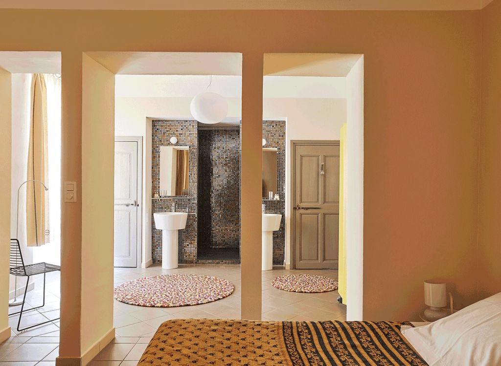 Elegant stone-walled French hotel room with antique wooden furniture, plush white linens, and soft natural light filtering through rustic window