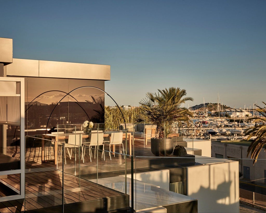 Luxurious white-themed penthouse suite with panoramic windows, minimalist design, king bed, and modern Barcelona skyline glimpse at sunset