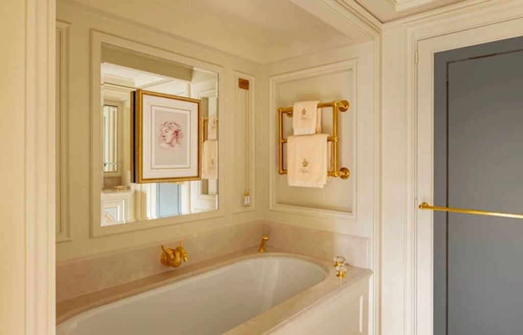 Opulent junior suite features gold-accented furniture, crystal chandelier, plush king bed with canopy, and antique writing desk with views of Paris