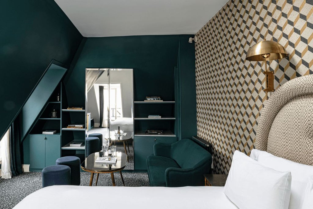 Elegant Parisian hotel room with rich burgundy walls, plush king bed, vintage brass fixtures, and large windows overlooking a charming street in the Grand Pigalle neighborhood