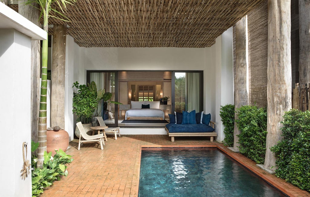 Elegant Thai resort facade with white colonial-style architecture, floor-to-ceiling windows and lush tropical gardens flanking entrance