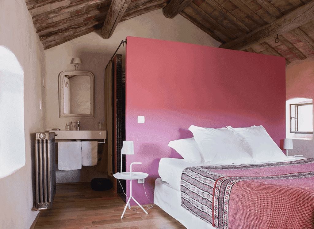 Elegant stone-walled bedroom with antique wooden furniture, soft white linens, and a charming French countryside view through rustic window