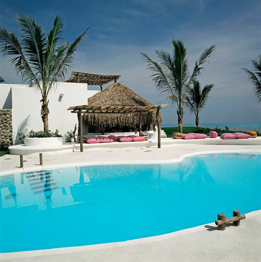 Luxurious white-washed Hotel Azúcar nestled against dramatic coastal cliffs with vibrant blue ocean and lush tropical vegetation in Puerto Escondido, Mexico