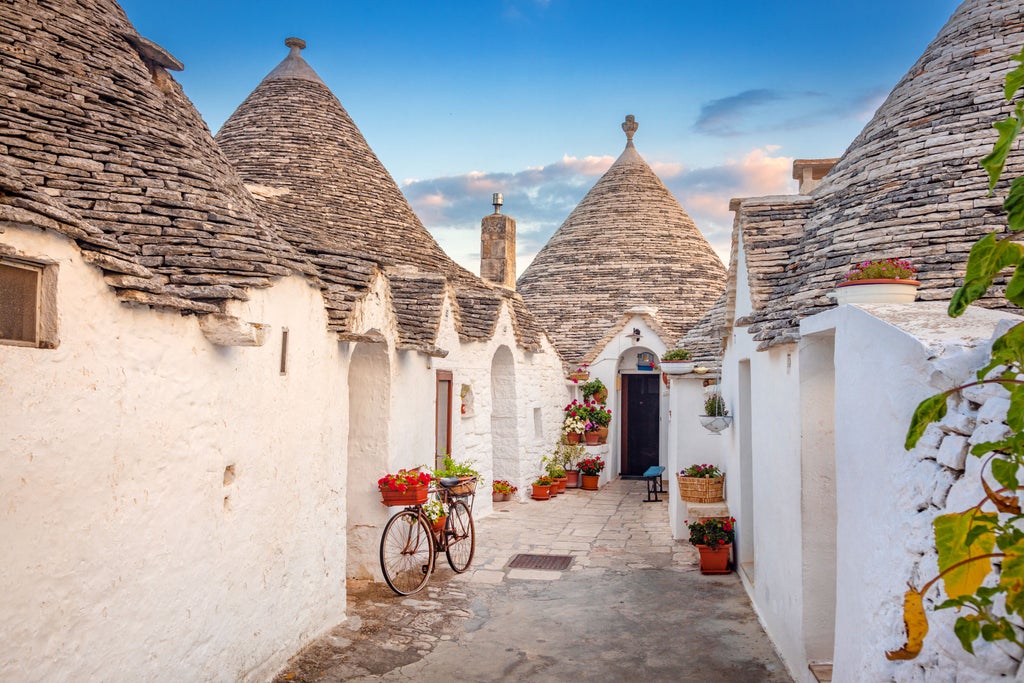 Traditional whitewashed trulli cottage with conical roof amidst olive trees, sunlit stone terrace and handcrafted mozzarella display