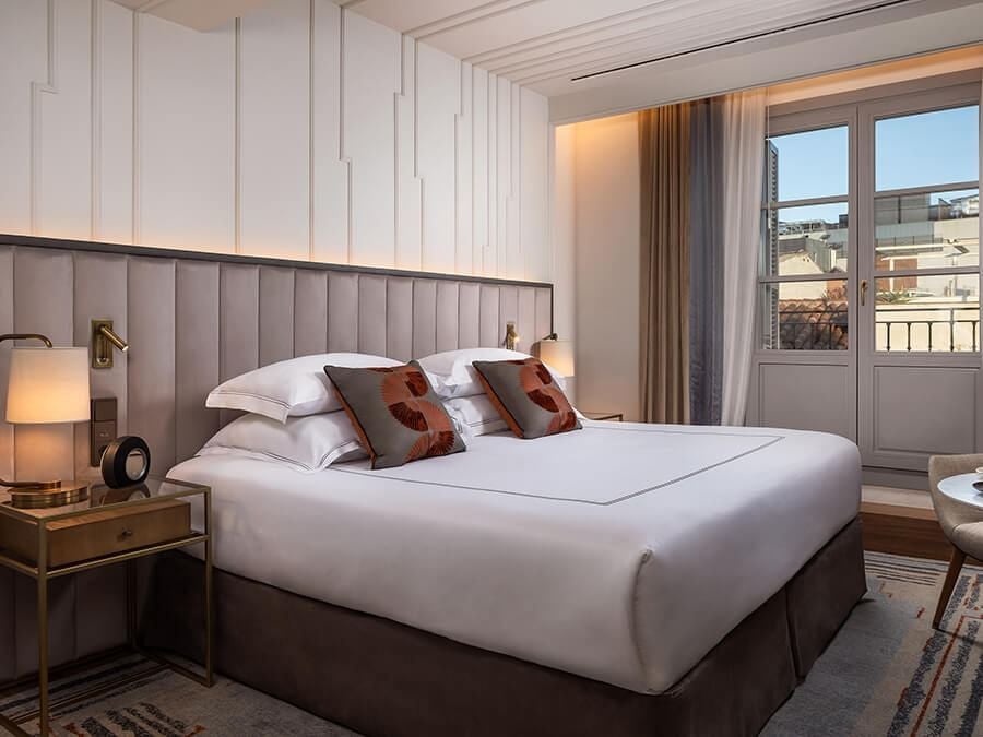 Elegant Spanish colonial-style hotel room with plush white bedding, ornate wooden furniture, and large windows in a luxurious Madrid boutique hotel