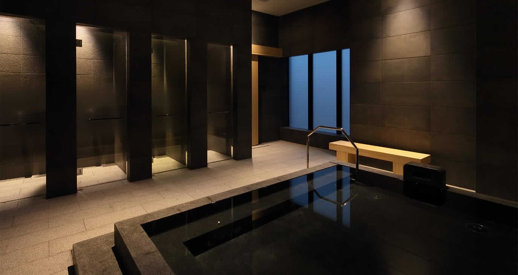 Contemporary luxury hotel entrance with minimalist stone facade, warm lighting, and traditional Japanese wood accents in central Kyoto