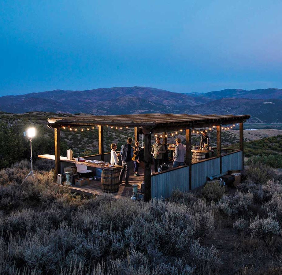 Luxurious mountain lodge featuring contemporary architecture with wooden and stone facade, nestled against dramatic snow-capped peaks at dusk