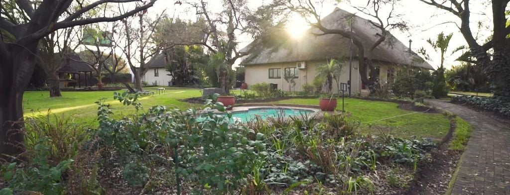 Elegant wooden deck overlooking African savanna at sunset, with infinity pool, luxury loungers and distant wildlife silhouettes