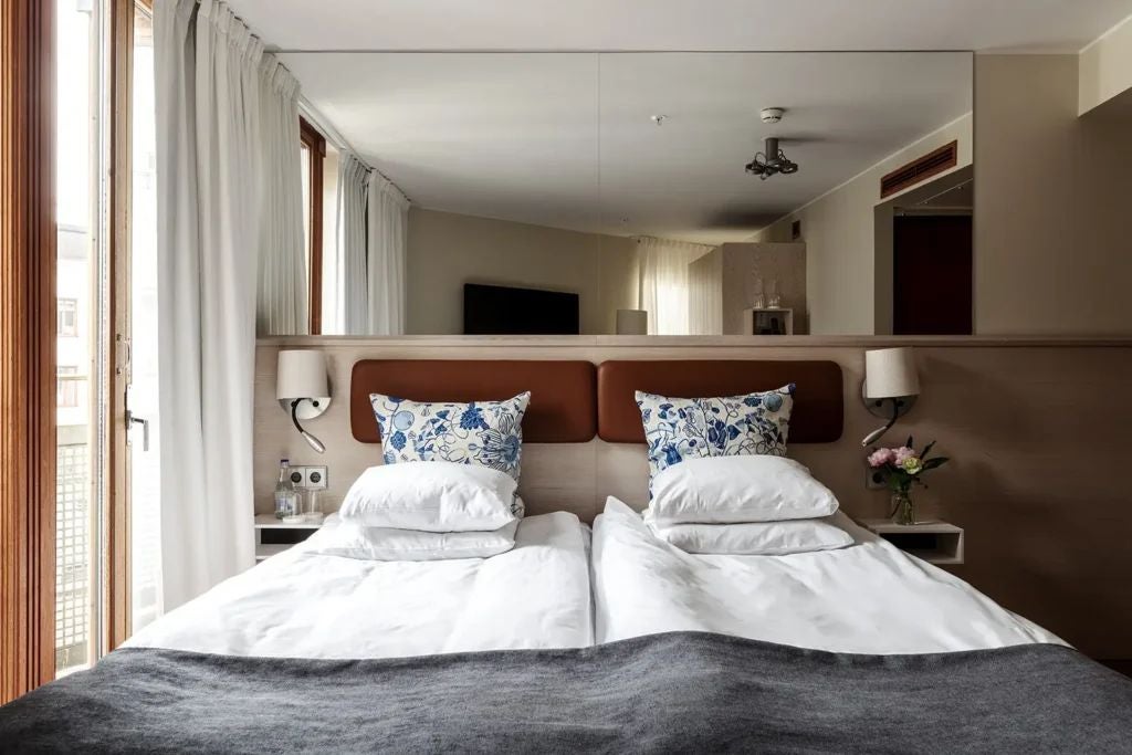 Elegant minimalist Swedish hotel room with soft neutral tones, plush white bedding, sleek modern furniture, and warm ambient lighting at Berns Hotel