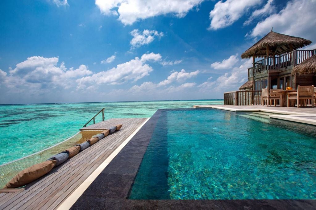 Overwater luxury villas with thatched roofs connected by wooden walkways over turquoise lagoon waters in the Maldives at sunset