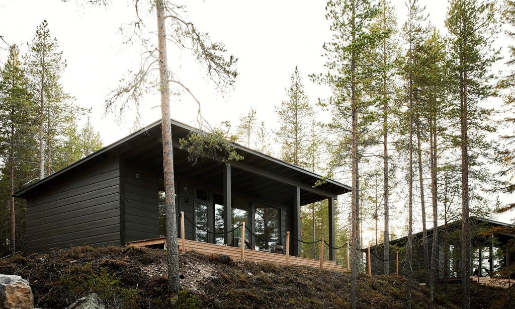 Modern Finnish luxury cabin with large panoramic windows overlooking snowy forest, featuring minimalist Nordic design and warm wooden interior at Arctic TreeHouse Hotel