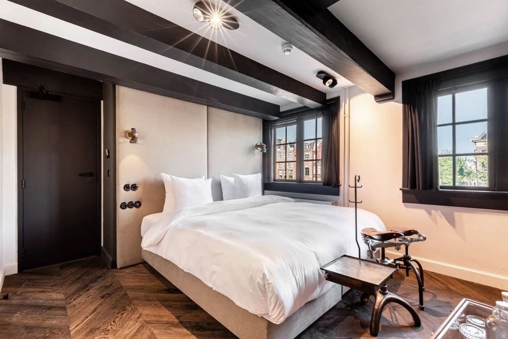 Stylish boutique hotel room featuring exposed wooden beams, plush king bed, canal views and antique bicycle-themed decor in Amsterdam