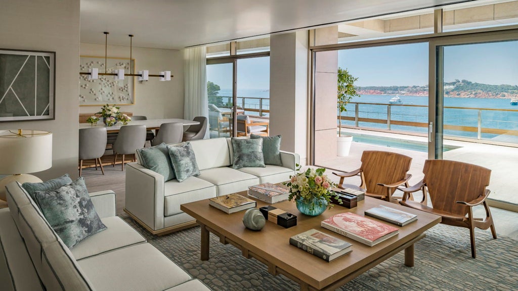 Opulent beachfront suite with floor-to-ceiling windows, modern furnishings, and panoramic Aegean Sea views from a private balcony.