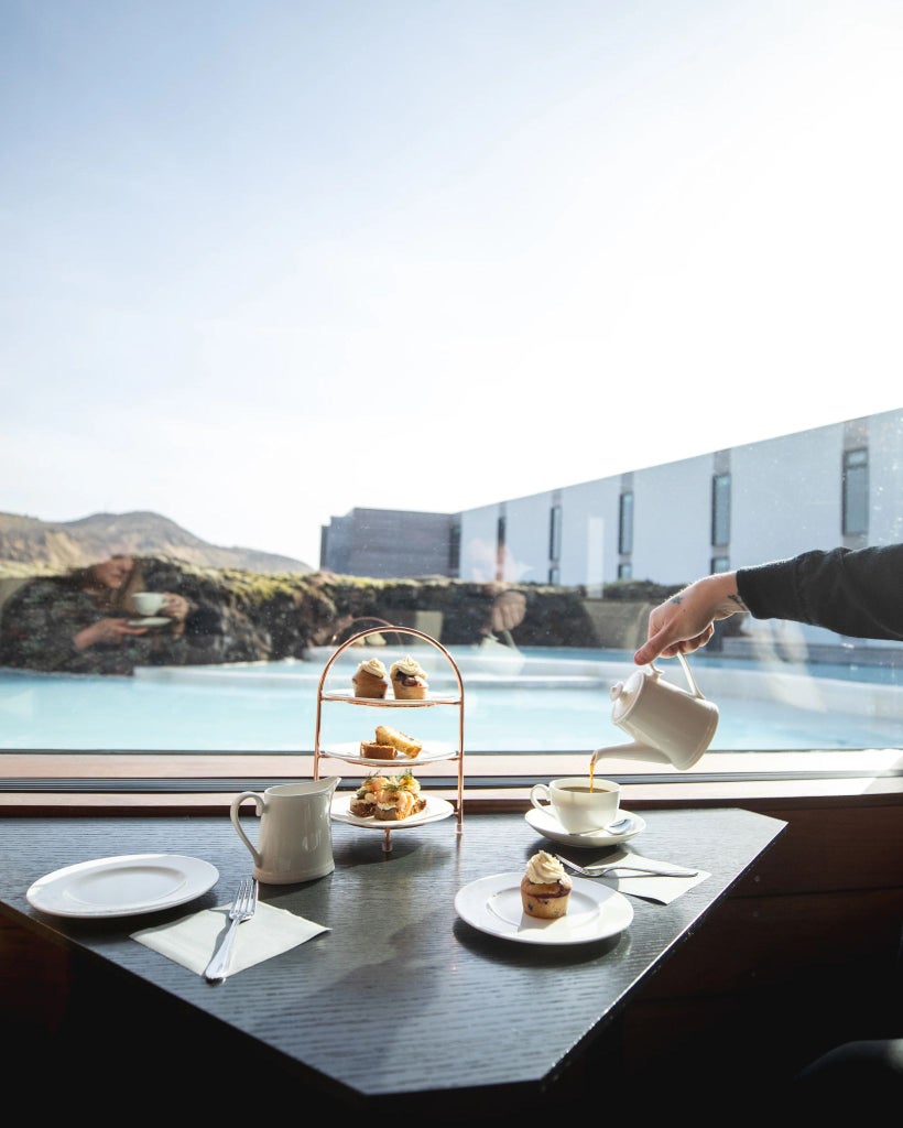 Luxurious minimalist scenset hotel nestled in rugged Icelandic landscape, featuring sleek glass walls reflecting dramatic volcanic terrain and soft evening light