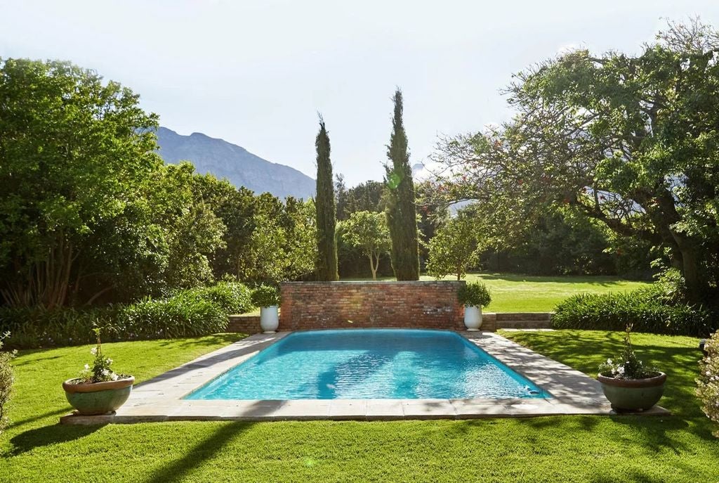 Elegant French-Colonial hotel nestled in Franschhoek Valley, with manicured gardens, stone facade and mountain backdrop