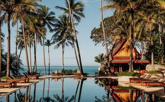 Luxurious Thai pavilions nestled on a palm-fringed hillside overlooking Andaman Sea, with traditional steep-pitched roofs and infinity pools