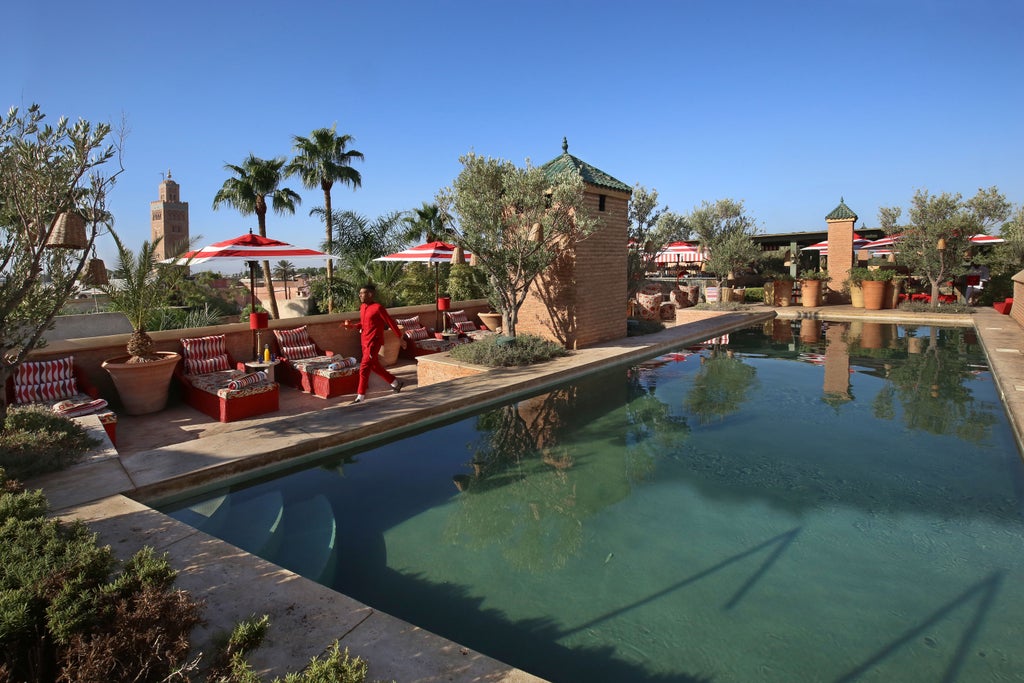 Elegant Moroccan riad courtyard featuring emerald-tiled pool, traditional archways, lush plants and cozy lounge seating at sunset