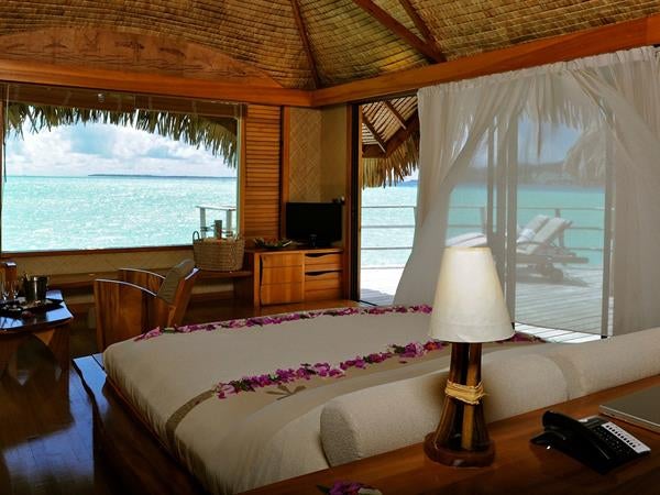 Luxurious overwater bungalow with private deck, floor-to-ceiling windows, turquoise lagoon views and thatched roof in French Polynesia