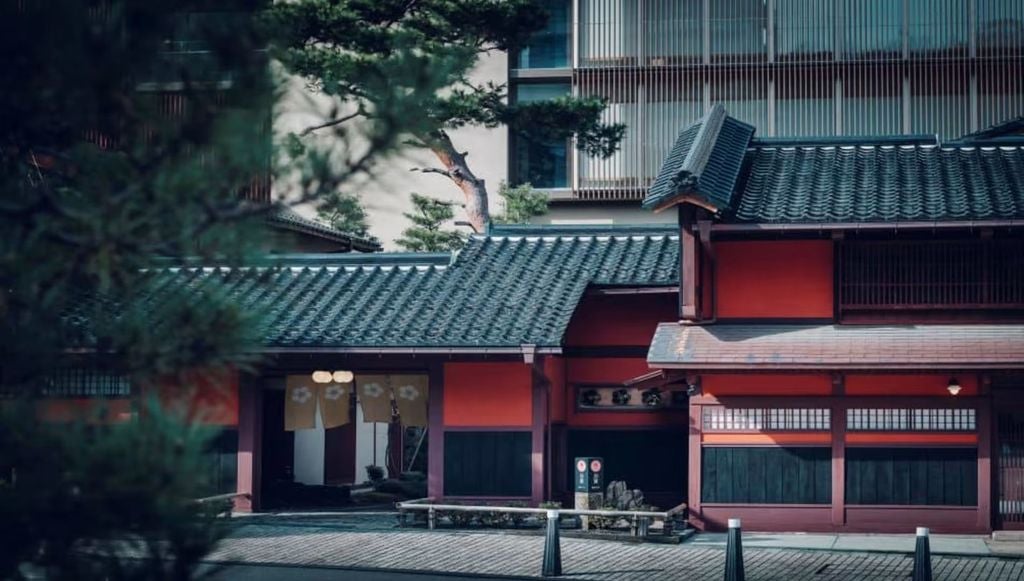 Traditional Japanese luxury ryokan with wooden facade, surrounded by lush gardens and lanterns along a stone path during sunset