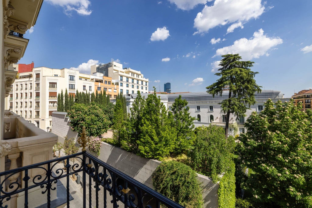 Elegant junior suite with plush white bedding, wooden floor, large windows overlooking Madrid's historic cityscape at URSO Hotel & Spa, showcasing refined Spanish hospitality