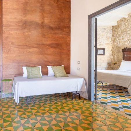 Elegant rustic Italian hotel room with stone walls, wooden furnishings, soft linen bedding, warm natural light filtered through traditional shutters