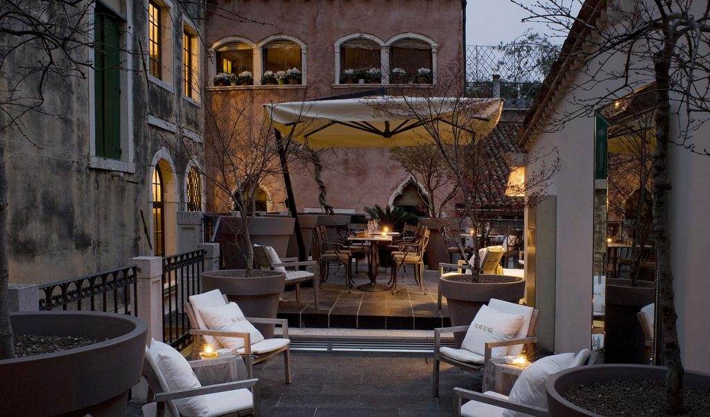 Elegant Venetian hotel facade with ornate marble details, grand arched windows, and wrought iron balconies overlooking a narrow canal