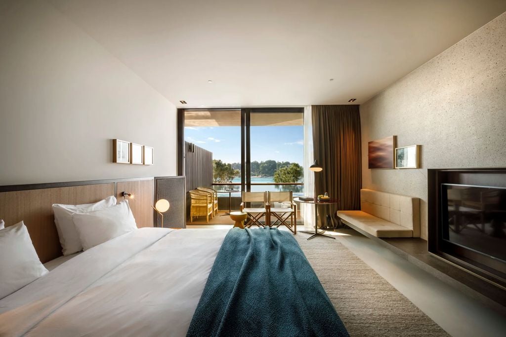 Modern luxury hotel room with floor-to-ceiling windows showcasing Adriatic Sea views, king bed, and minimalist wood furnishings