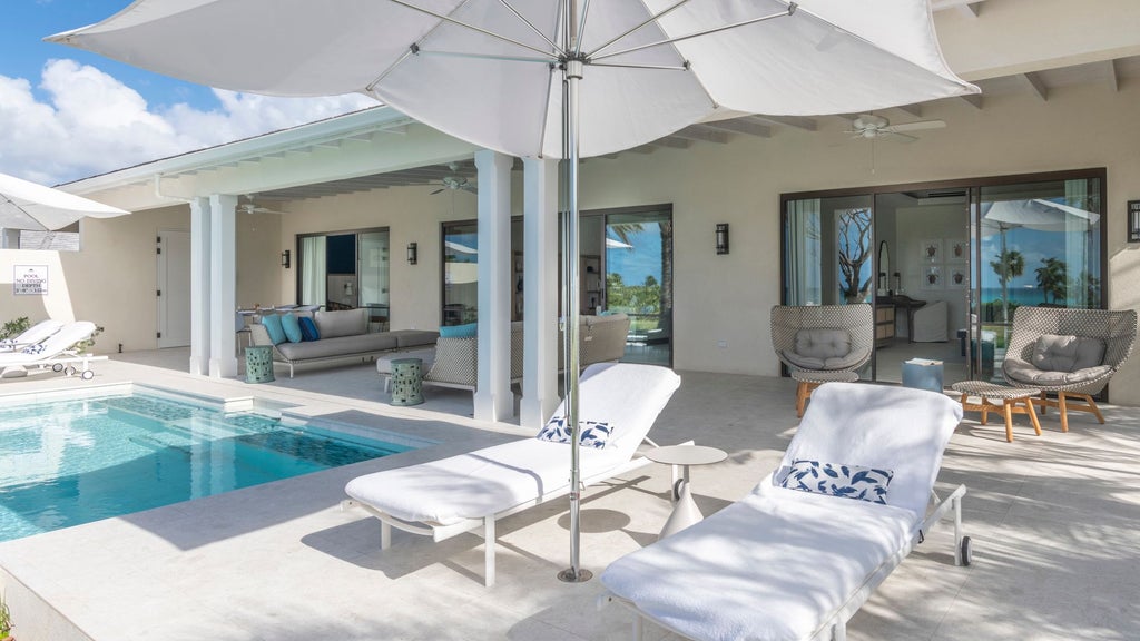 Luxurious family suite at Jumby Bay Island resort, featuring elegant Caribbean-style decor, plush king bed, and panoramic ocean view through sliding glass doors.