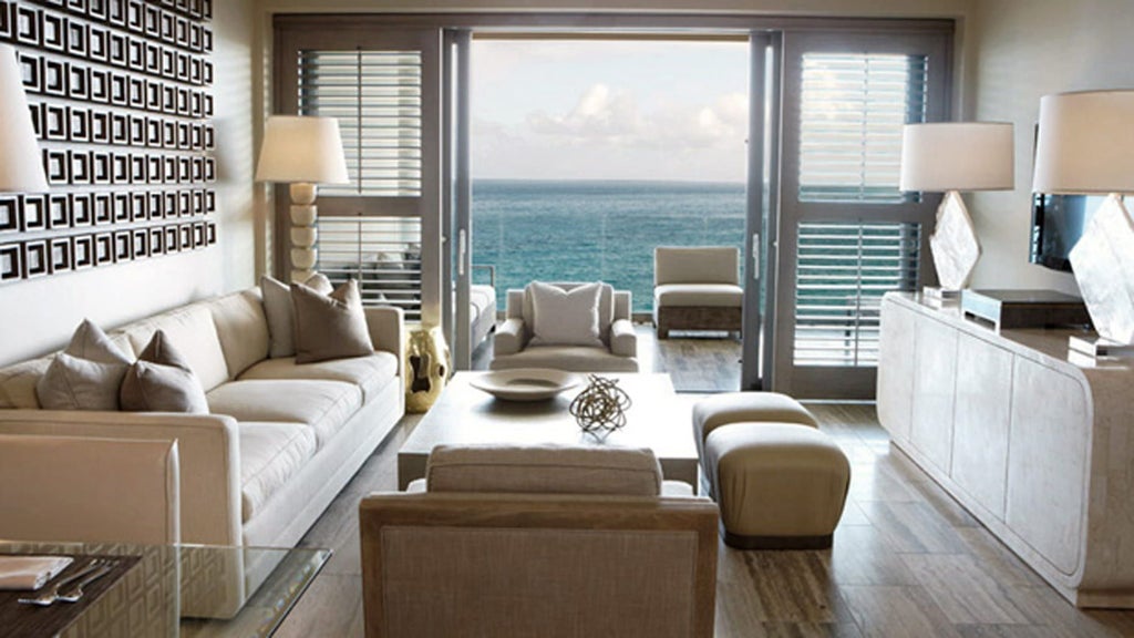 Spacious beachfront suite with king bed, floor-to-ceiling windows, private balcony, and modern furnishings overlooking Caribbean Sea