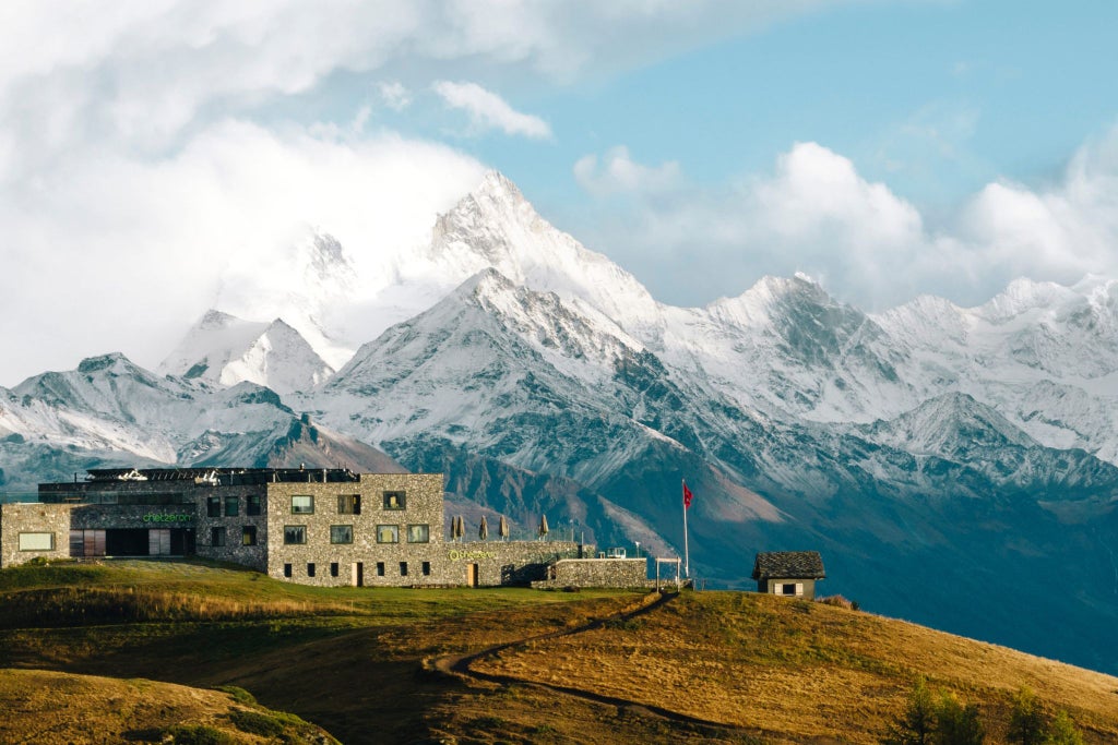 Luxurious alpine hotel Chetzeron perched on rocky mountainside, panoramic Swiss Alps view, modern concrete architecture blending with rugged terrain