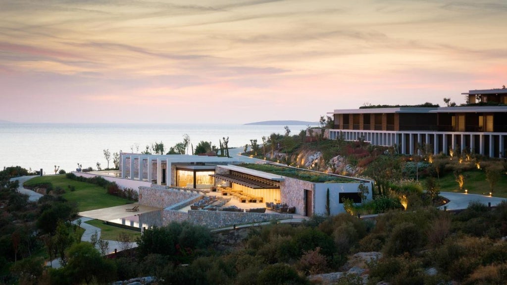 Modern seaside resort nestled in rugged Turkish cliffs overlooking turquoise Aegean Sea, featuring infinity pools and terraced architecture