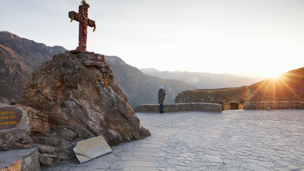 Luxury stone cottages with thatched roofs nestled in lush Andean mountainside, overlooking Sacred Valley's misty peaks at sunset