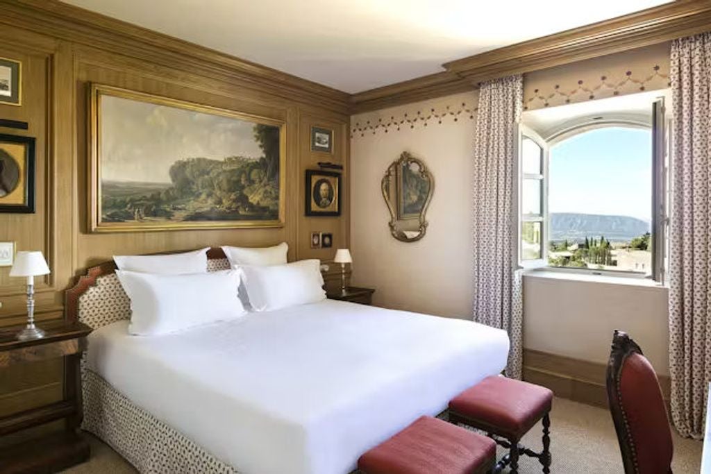 Elegant hotel room with panoramic valley views featuring classic French decor, king bed, crystal chandelier and antique furnishings