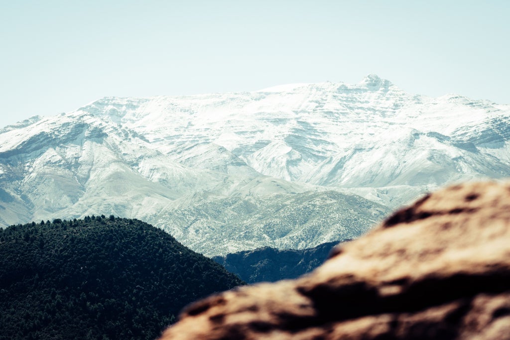 Panoramic view of rugged Atlas Mountains with Berber hikers in traditional attire traversing rocky terrain near Marrakech, Morocco's dramatic landscape unfolding