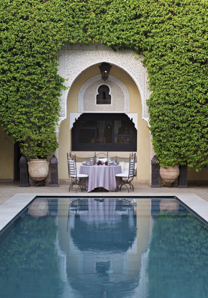 Luxurious Moroccan riad courtyard with central fountain, terra cotta planters, ornate archways and traditional lanterns at dusk