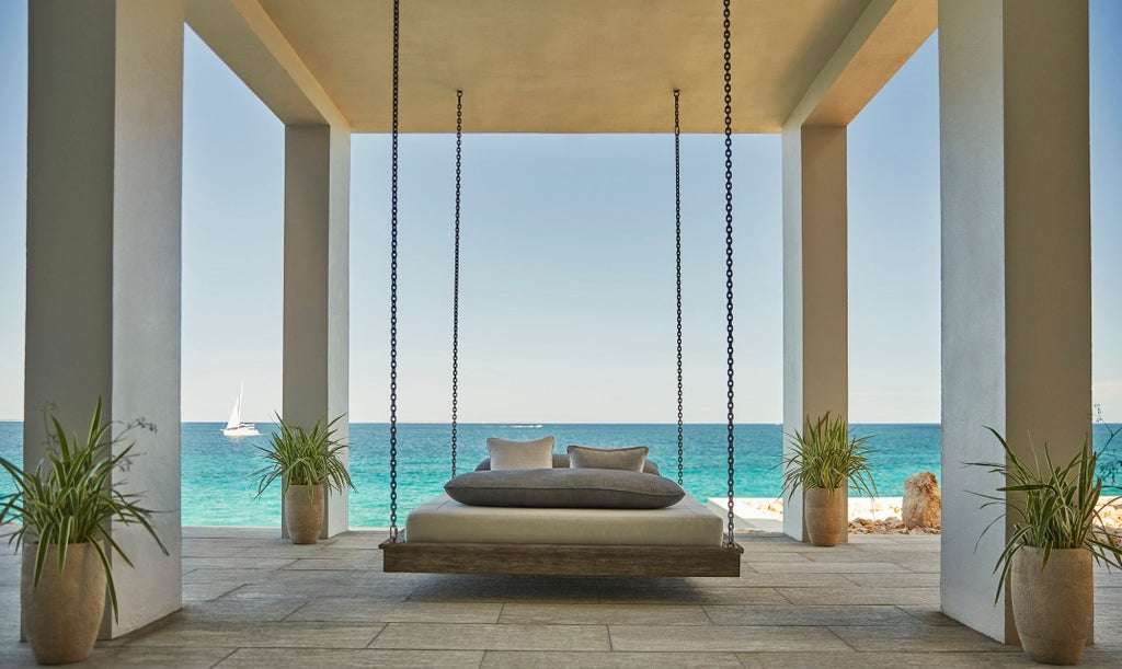 Infinity-edge pool overlooking Caribbean Sea at sunset, flanked by palm trees and modern lounge chairs at Four Seasons Anguilla resort