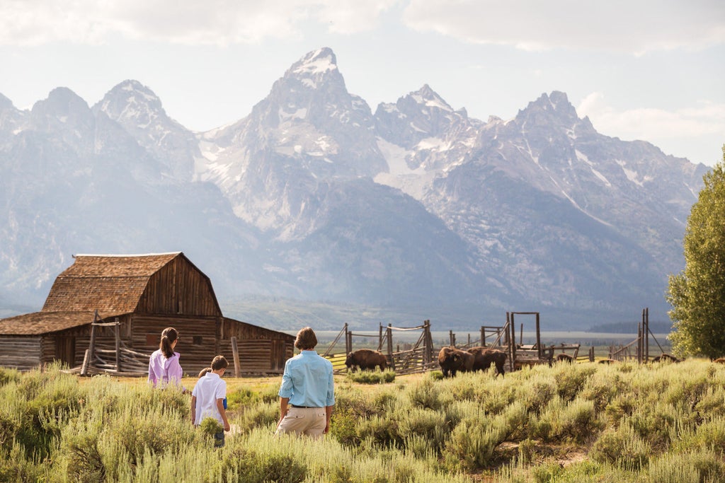 Luxurious mountain lodge hotel with stone and timber façade nestled against snow-capped Teton peaks at sunset in Wyoming wilderness