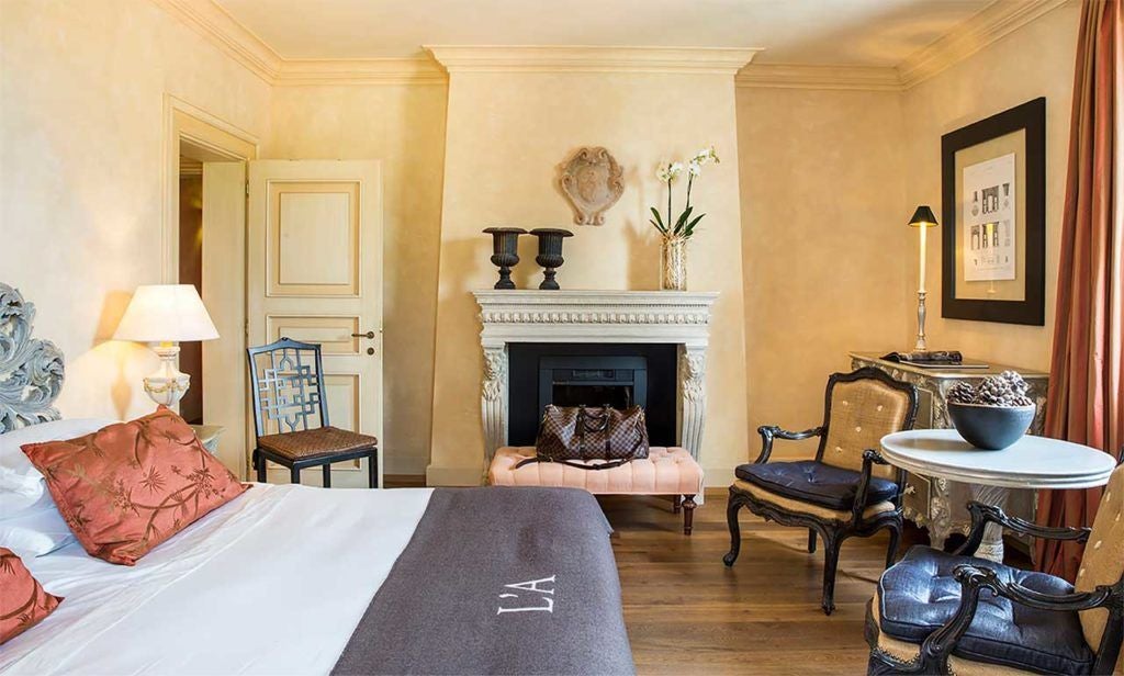 Elegant Superior Room at L'Andana, featuring plush white bedding, rustic wooden furniture, and soft natural light streaming across Tuscan-inspired decor