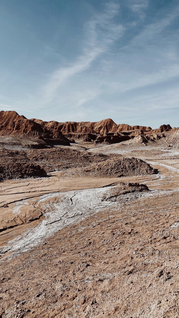 Expansive Atacama Desert landscape showing red sand dunes meeting dramatic mountains under clear blue skies at golden hour