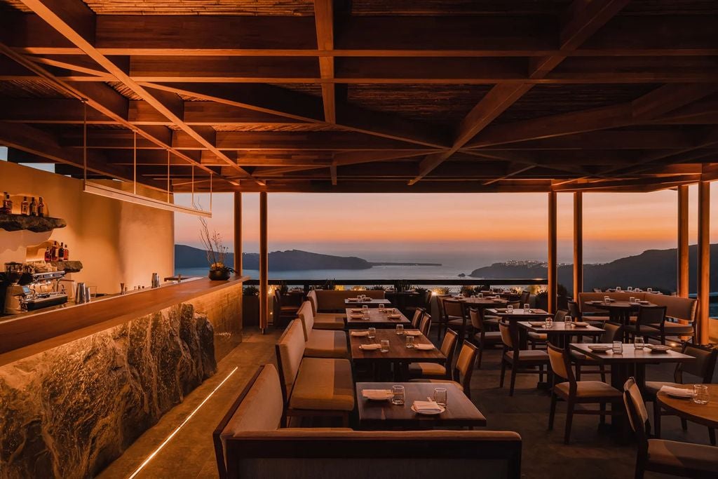 Sleek infinity pool overlooking Santorini's caldera at sunset, with minimalist white architecture and private cabanas framing the sea view