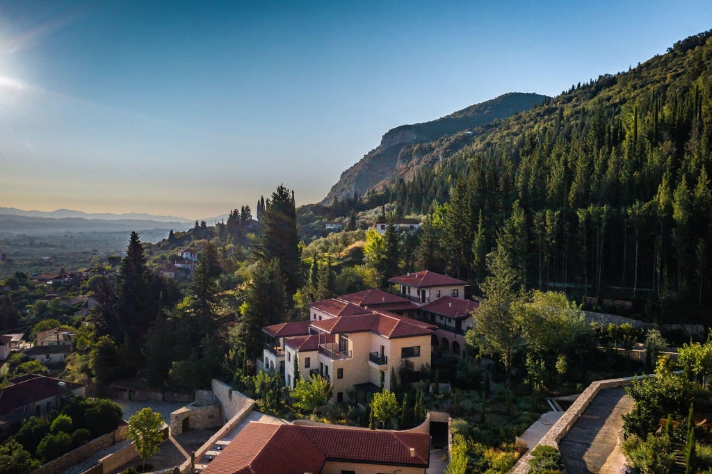 Modern stone and glass wellness resort nestled in Greek hillside, featuring infinity pool overlooking misty mountain landscape at sunset