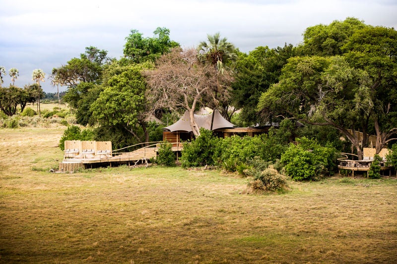 Elevated safari lodge deck overlooking lush Okavango Delta with plush lounge chairs, thatched roof, and panoramic savanna views at sunset