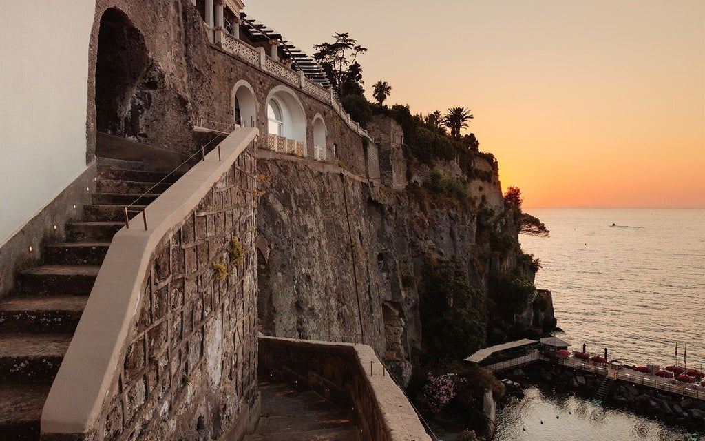 Luxurious Mediterranean hotel perched on Sorrento cliffs, featuring elegant white architecture, azure sea views, and lush green terraces overlooking the coastline