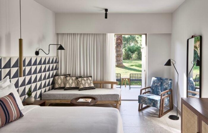 Luxurious Phāea Cretan Malia bungalow garden view room with modern decor, crisp white linens, and elegant wooden furnishings overlooking lush Mediterranean greenery