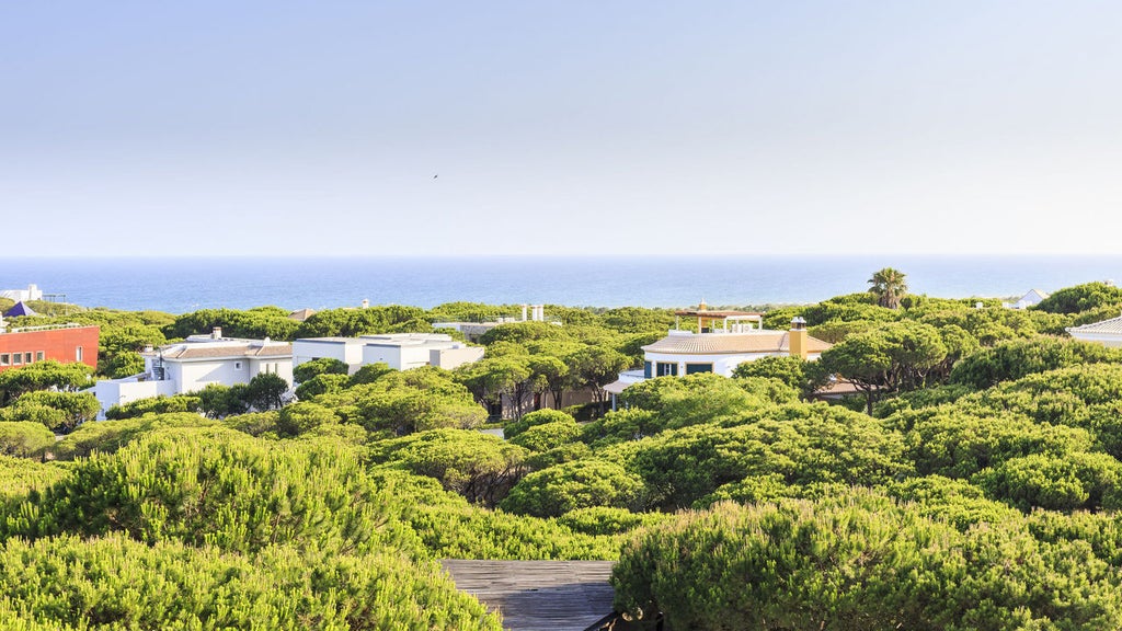 Contemporary beachfront hotel with sleek white architecture, surrounded by lush pine forest and overlooking pristine sandy beach in Portugal