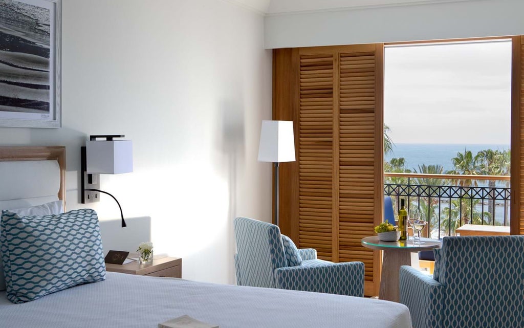 Elegant sea-view hotel room with modern decor, panoramic windows overlooking azure Mediterranean coastline, crisp white linens and minimalist design