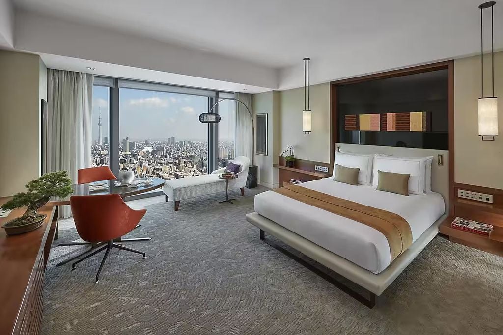 Elegant hotel room overlooking Tokyo skyline with floor-to-ceiling windows, king bed, modern furnishings and marble bathroom vanity