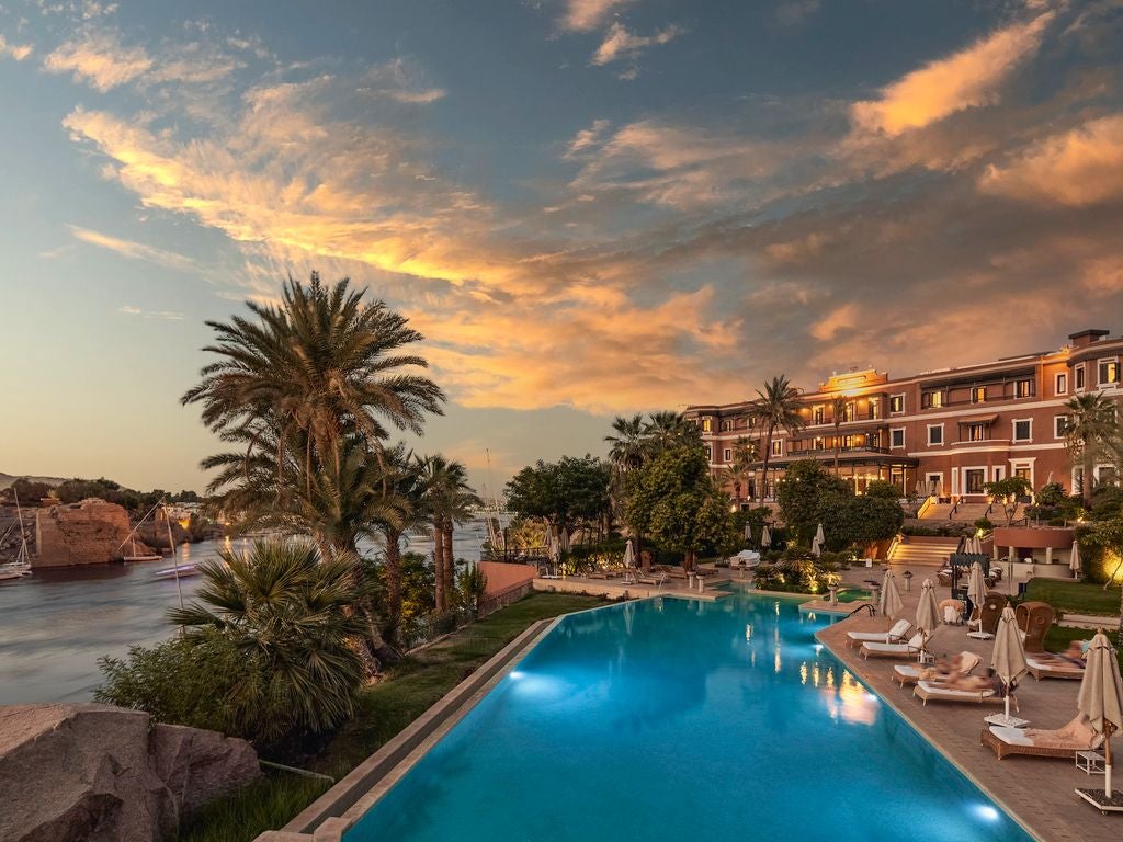 Luxurious historic hotel overlooking the Nile River, with elegant colonial architecture, lush gardens, and a grand terrace at sunset in Aswan, Egypt